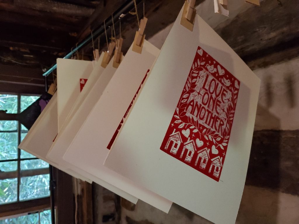 linocuts hanging in a rack with 'love one another' design