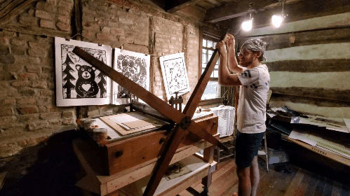 artist dustin cecil using the press at the log cabin print shop