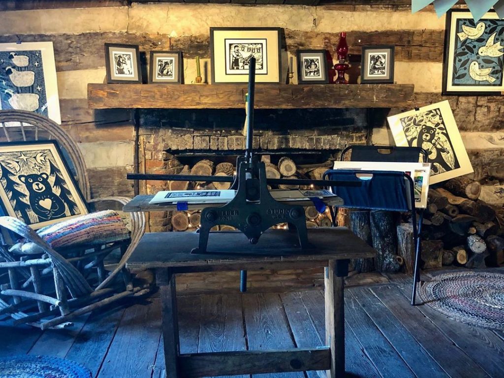 interior photo of the log cabin print shop in old washington kentucky antique press in the foreground logs and artwork in the background