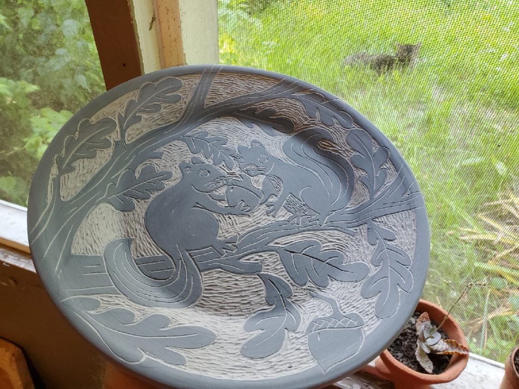 an unfired pottery plate with two decorative squirrels