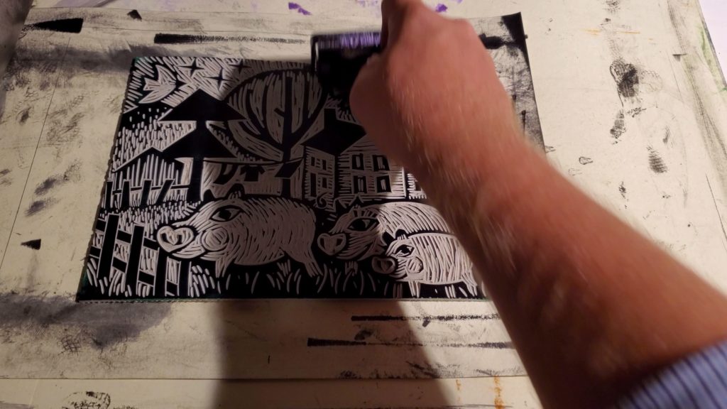 hand inking a linocut print of pigs in mud