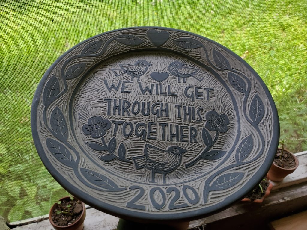 an unfired pottery plate, with a decoration saying, we will get through this together