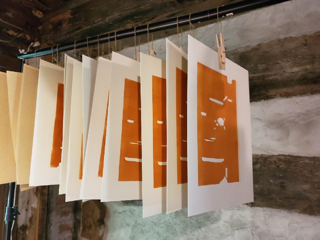 orange prints hanging in an improvised drying rack