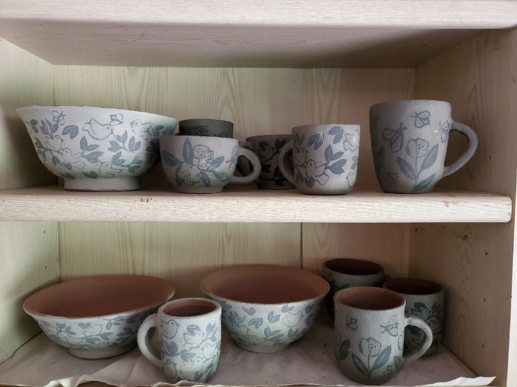 2 shelves with bowls and mugs ready to be fired