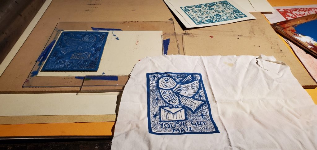 linocut block print on fabric depicting a bird carrying a letter with the words: you've got mail